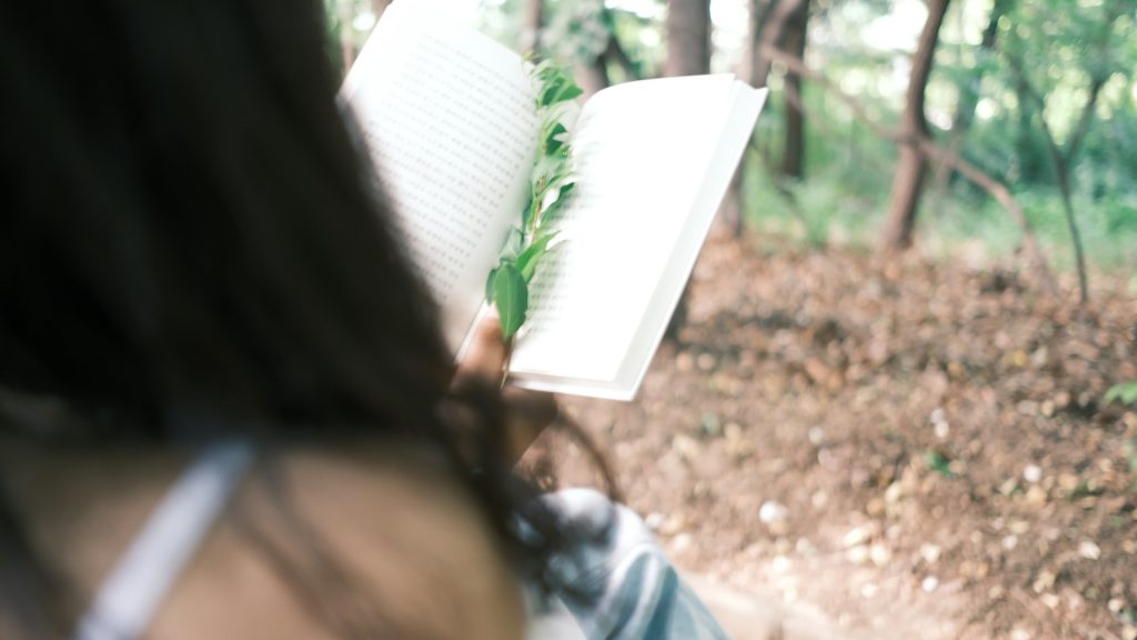 Una chica lee en un bosque, la vista es desde detrás de ella